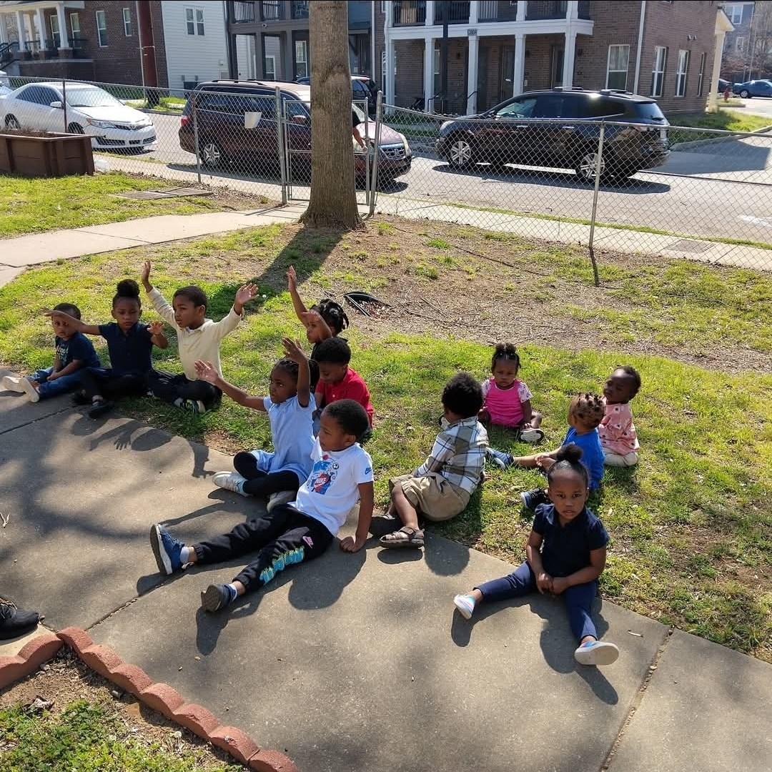 Children from Bridging the Gap Learning Center sitting together outside on a sunny day