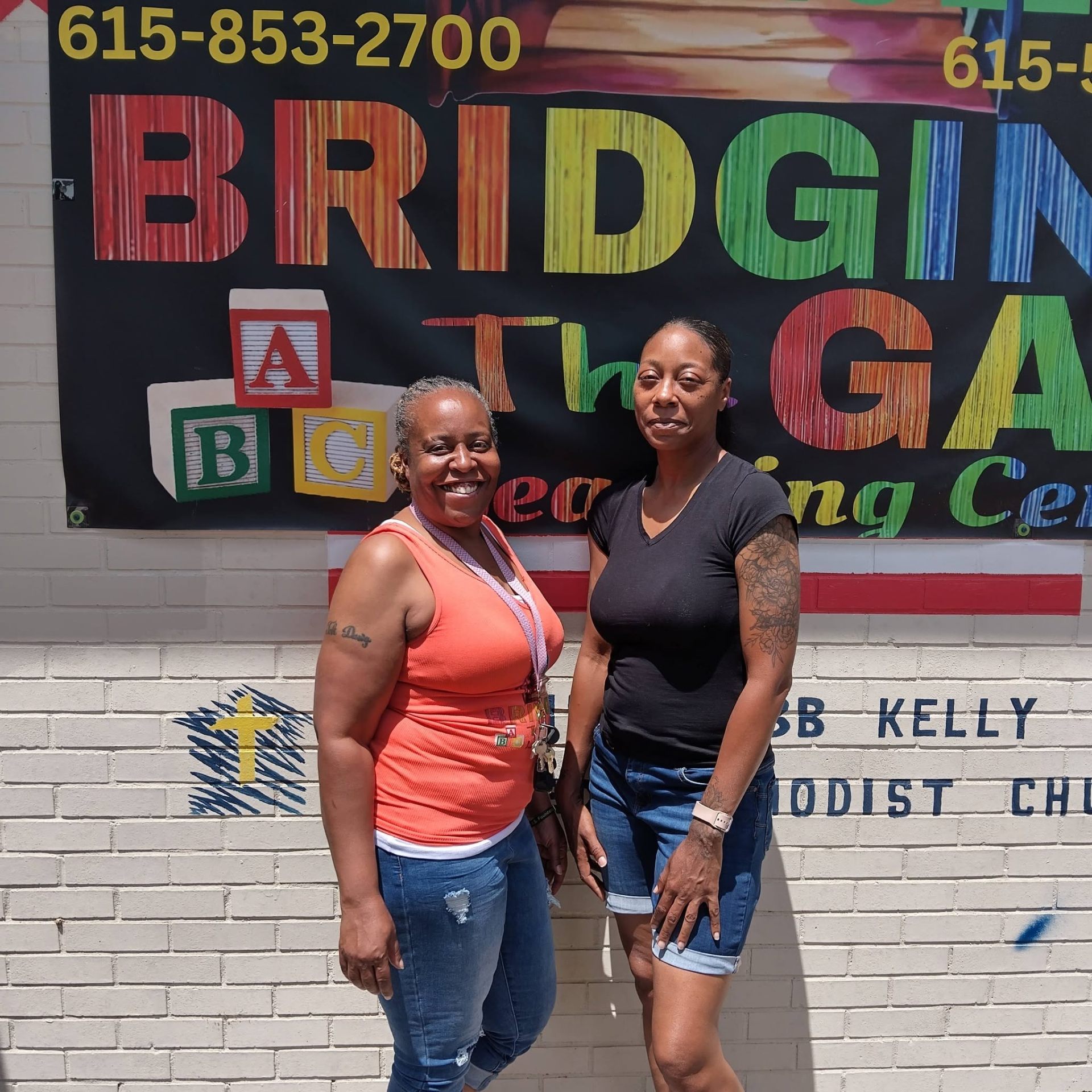 Miss Tika and a colleague in front of the Bridging the Gap Learning Center banner